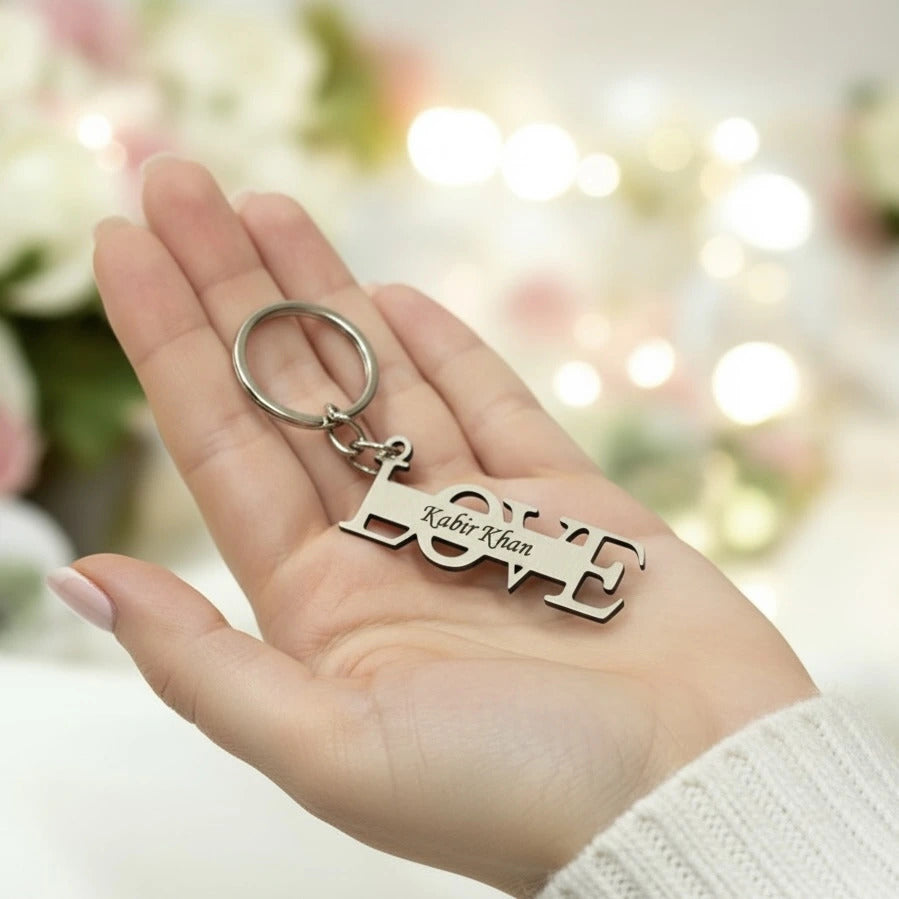 Hand holding a keychain with 'Kabir Khan' engraved, against a blurred floral background