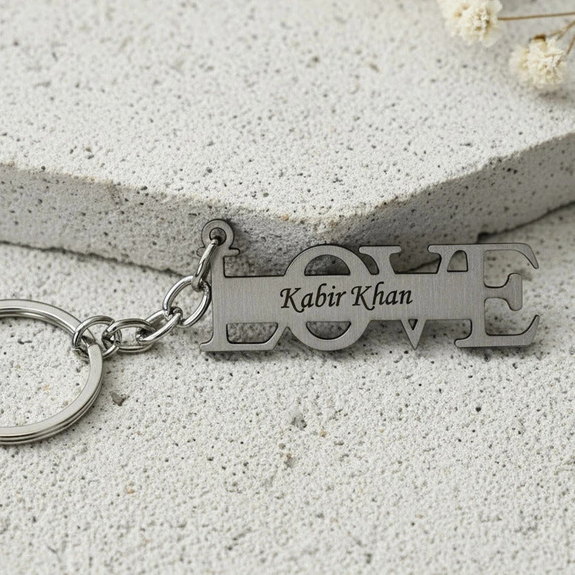 Silver keychain with 'LOVE' and engraved name on a light stone surface