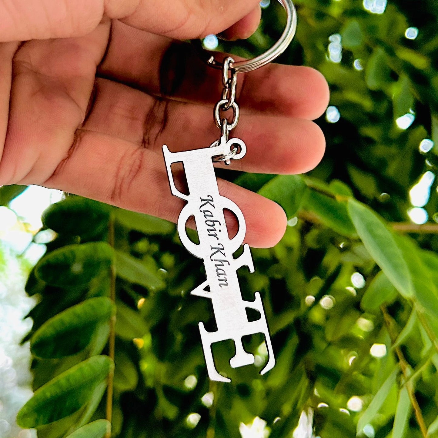 Keychain with personalized design held by a hand against a green leafy background