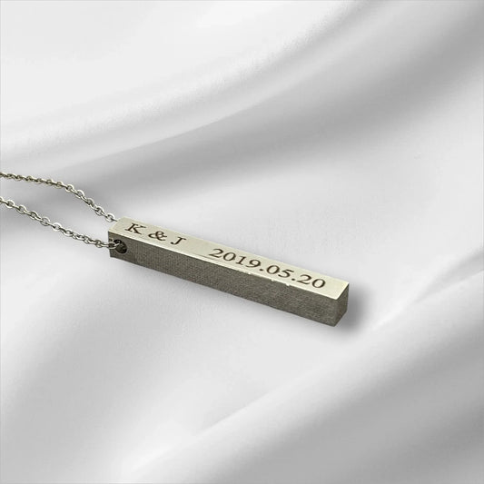 Bar-shaped necklace with engraved initials and date on a light gray background