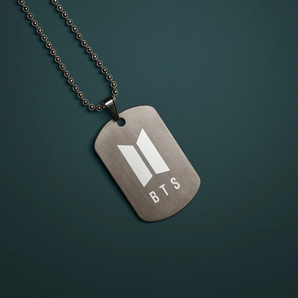 Metallic dog tag necklace with BTS logo on a dark green background