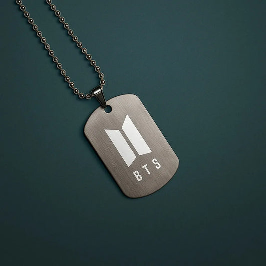 Metallic dog tag necklace with BTS logo on a dark green background