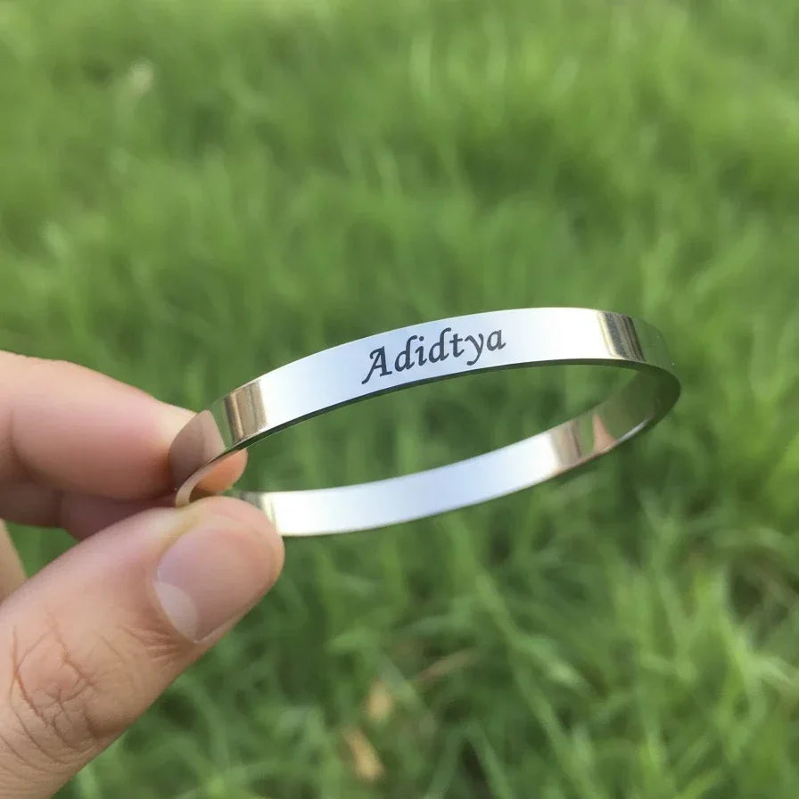 Silver bracelet with engraved name held against a grassy background