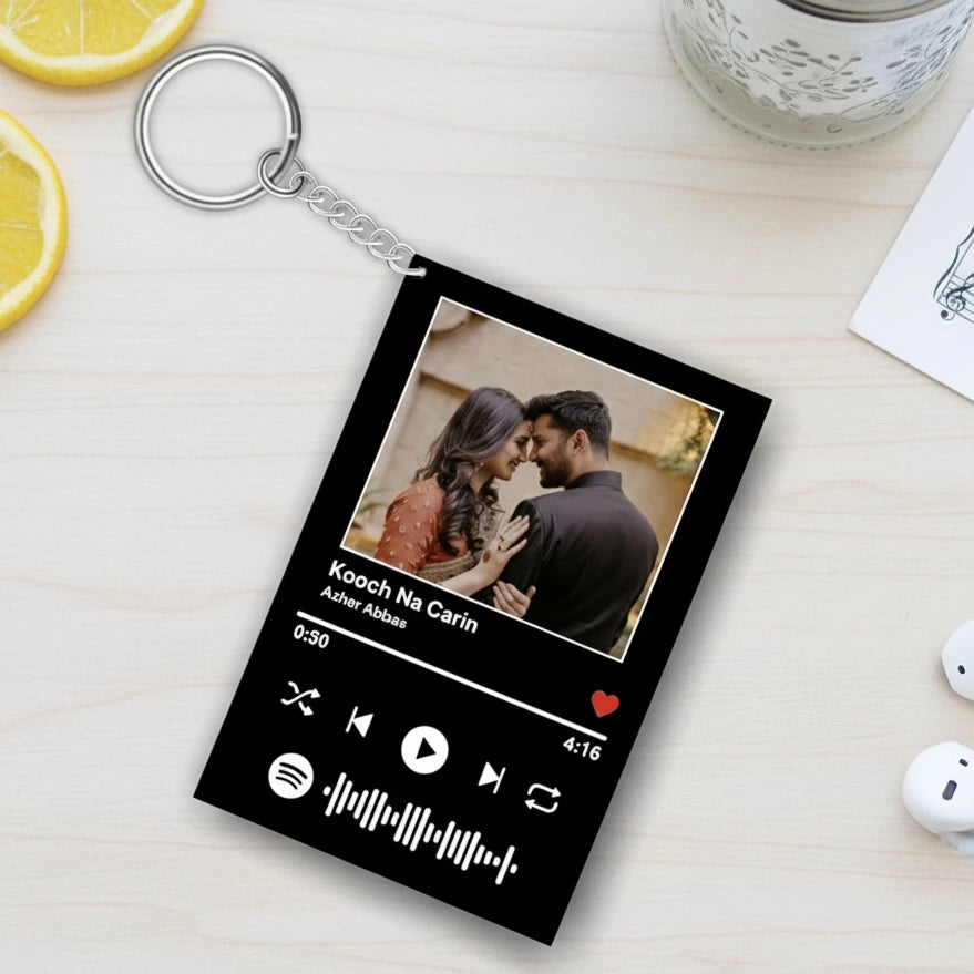 Keychain with a personalized design of a couple and music player interface on a light wooden surface.