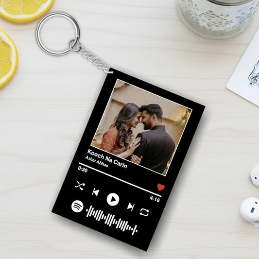 Keychain with a personalized design of a couple and music player interface on a light wooden surface.