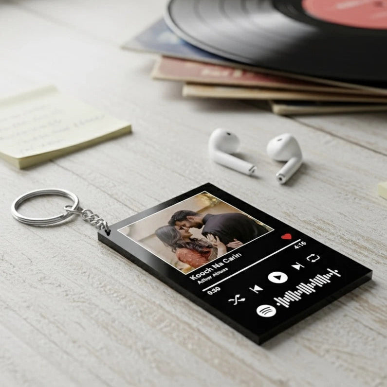 Keychain with music player design and couple photo on a wooden surface with earbuds and vinyl records.