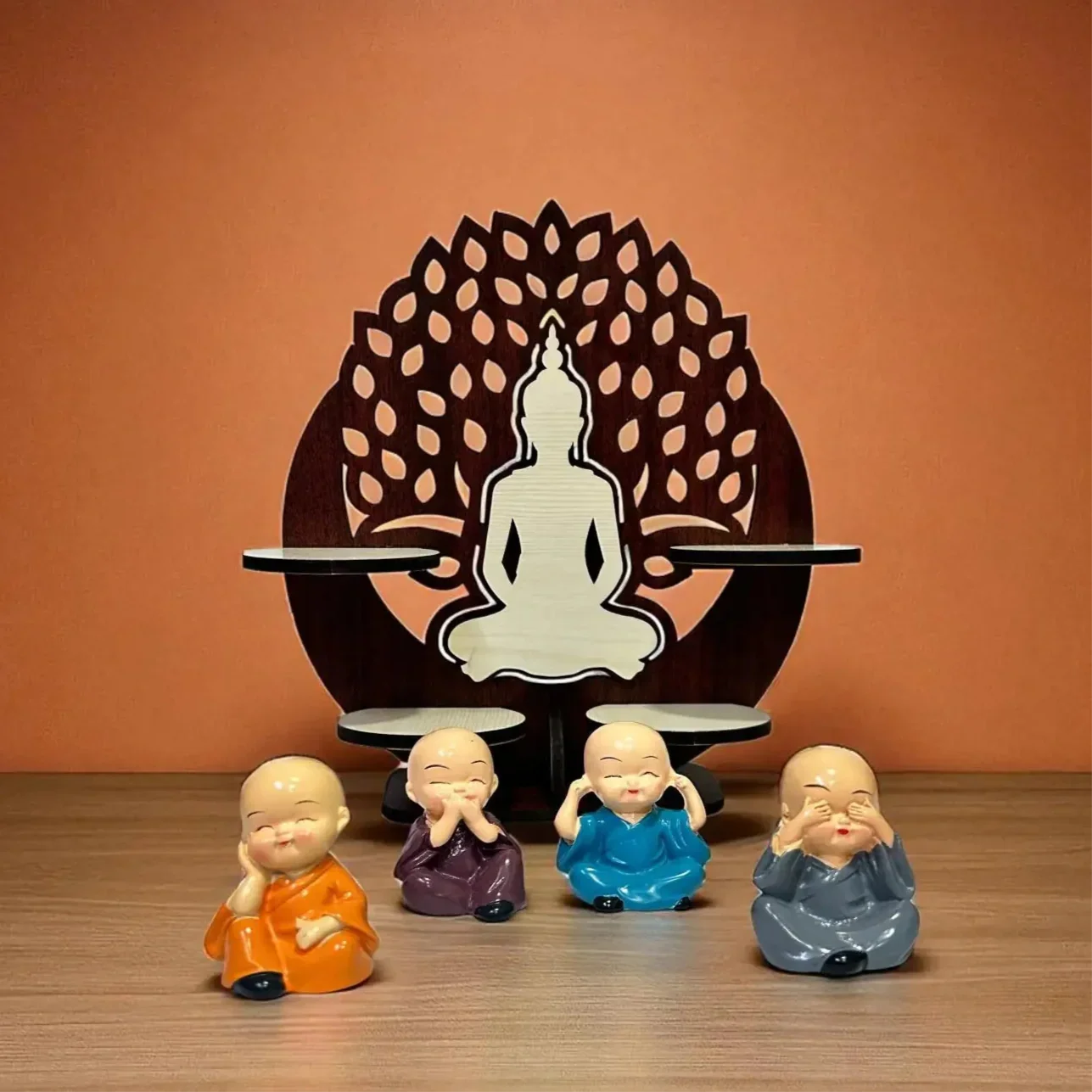 Set of four colorful monk figurines in front of a Buddha statue with lotus design on an orange background