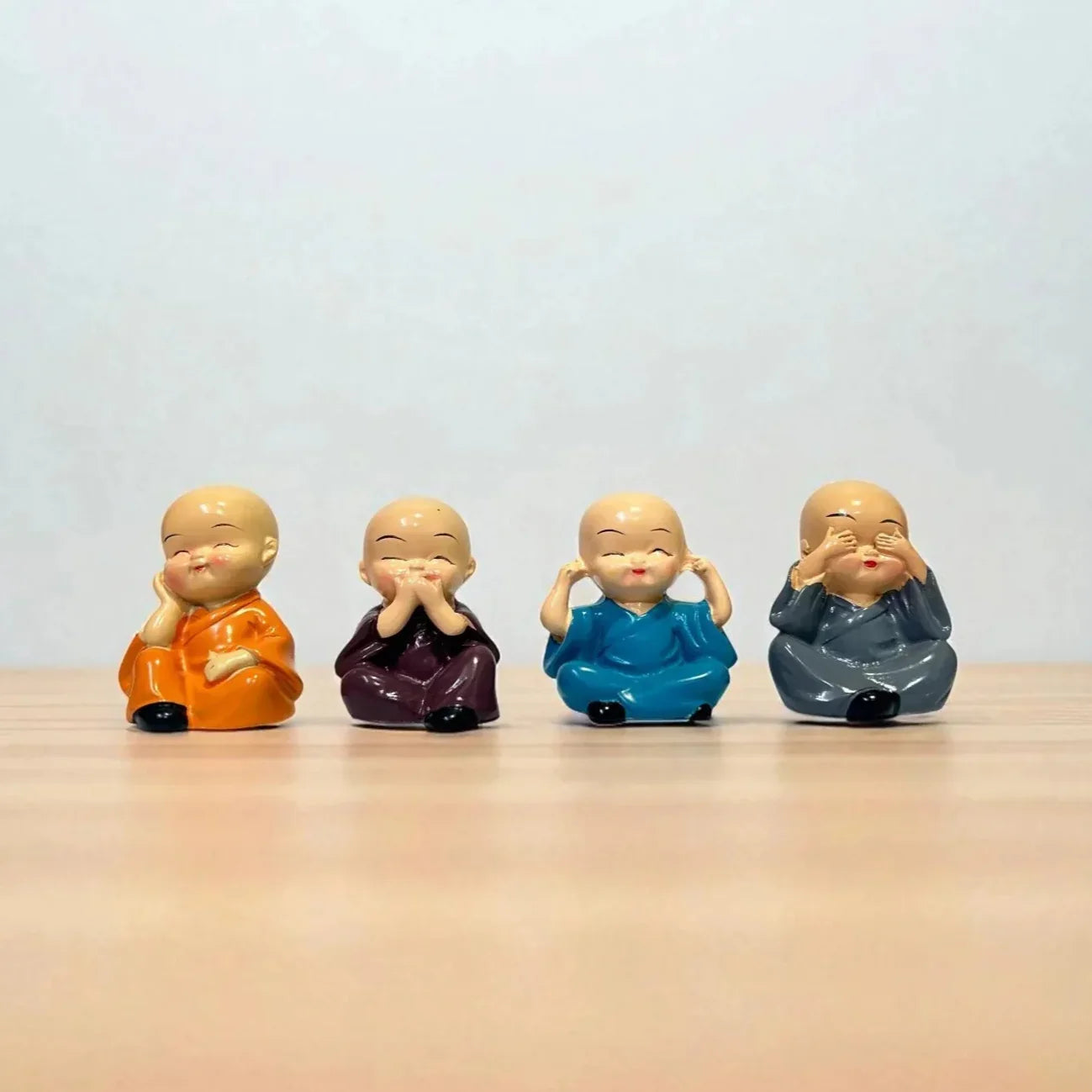 Four small figurines of a monk in different colors on a wooden surface with a light gray background