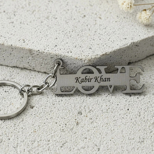 Silver keychain with 'LOVE' and engraved name on a light stone surface