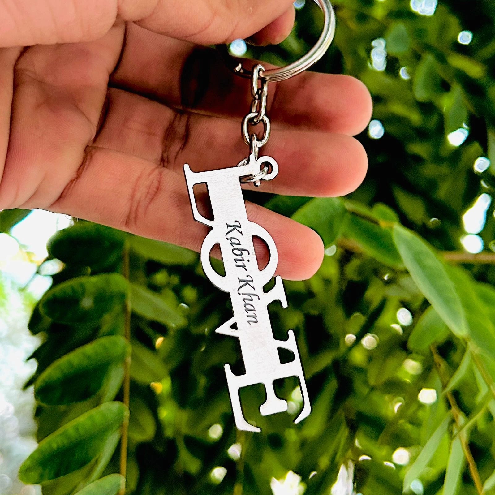 Keychain with personalized design held by a hand against a green leafy background