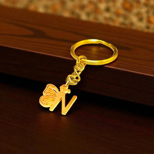 Gold keychain with butterfly and letter 'N' on a wooden surface