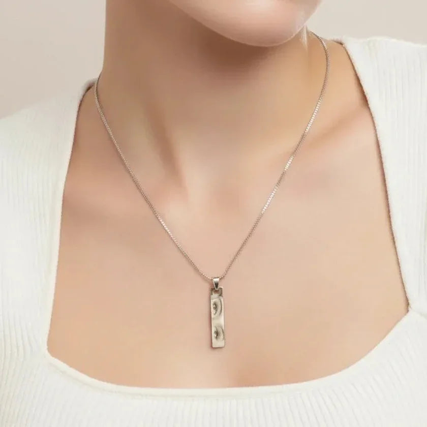 engraved metal bar pendant close-up Silver necklace with a pendant on a mannequin wearing a white top.
