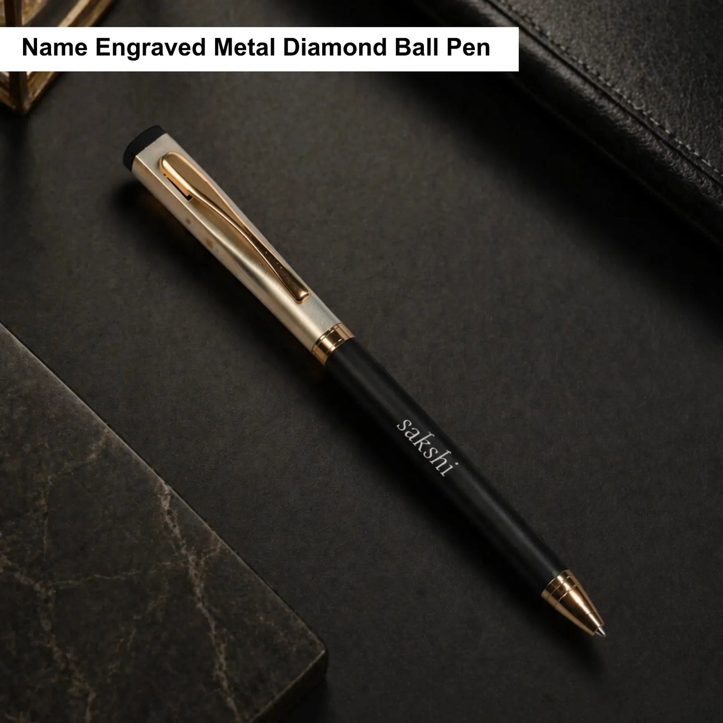Black and gold pen with 'sakshi' branding on a dark surface