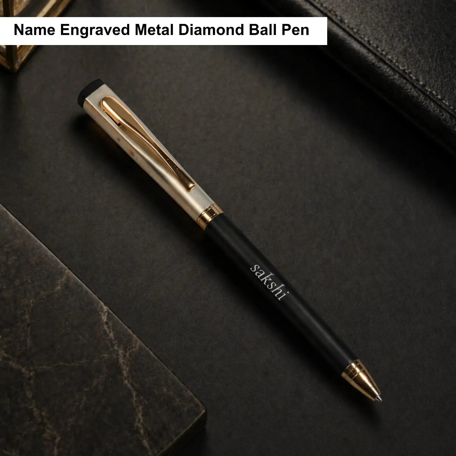 Black and gold pen with 'sakshi' branding on a dark surface