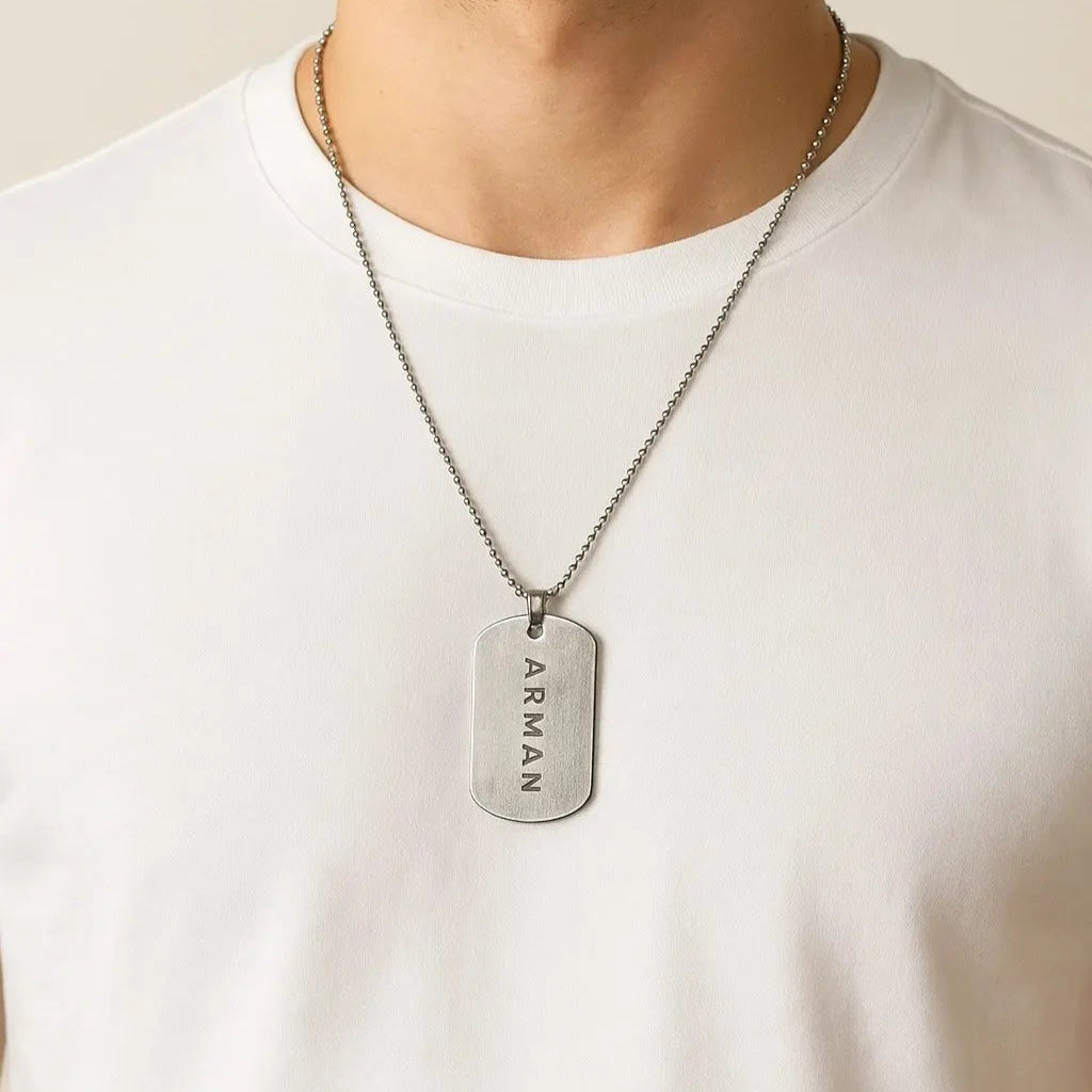 Man wearing a silver Armani dog tag necklace on a plain background